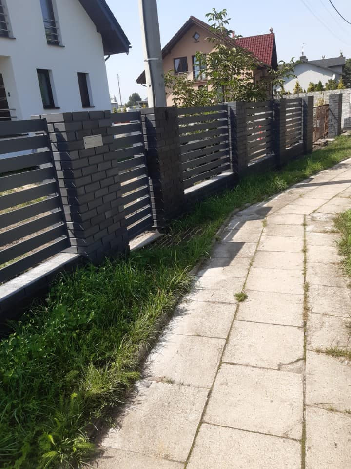 Nowoczesne ogrodzenie z szarej cegły i poziomych paneli w Kamyku, widok z chodnika.