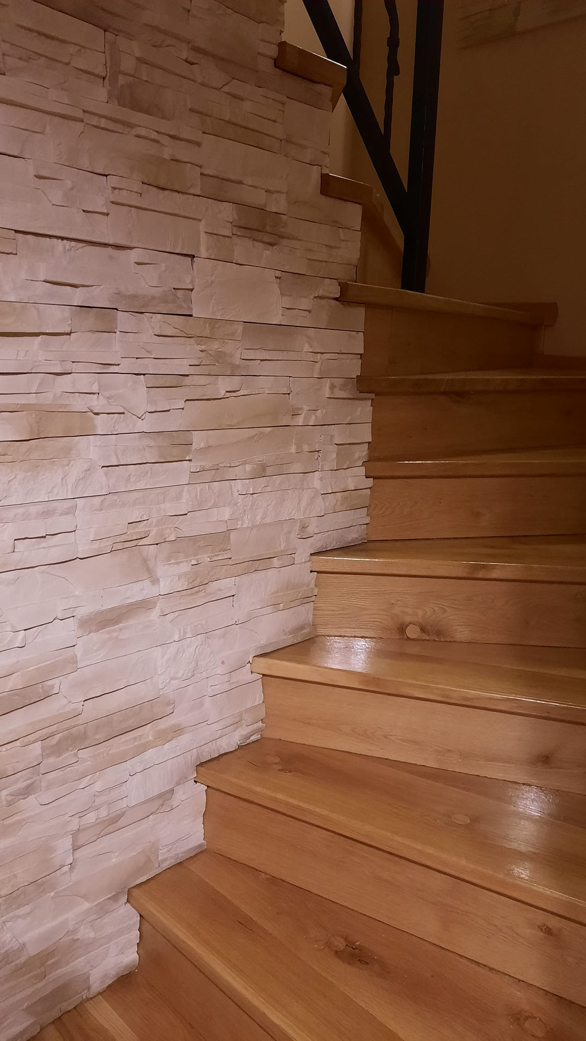 Wykończenie klatki schodowej z drewnianymi schodami i ścianą wyłożoną dekoracyjnym kamieniem w odcieniach beżu.