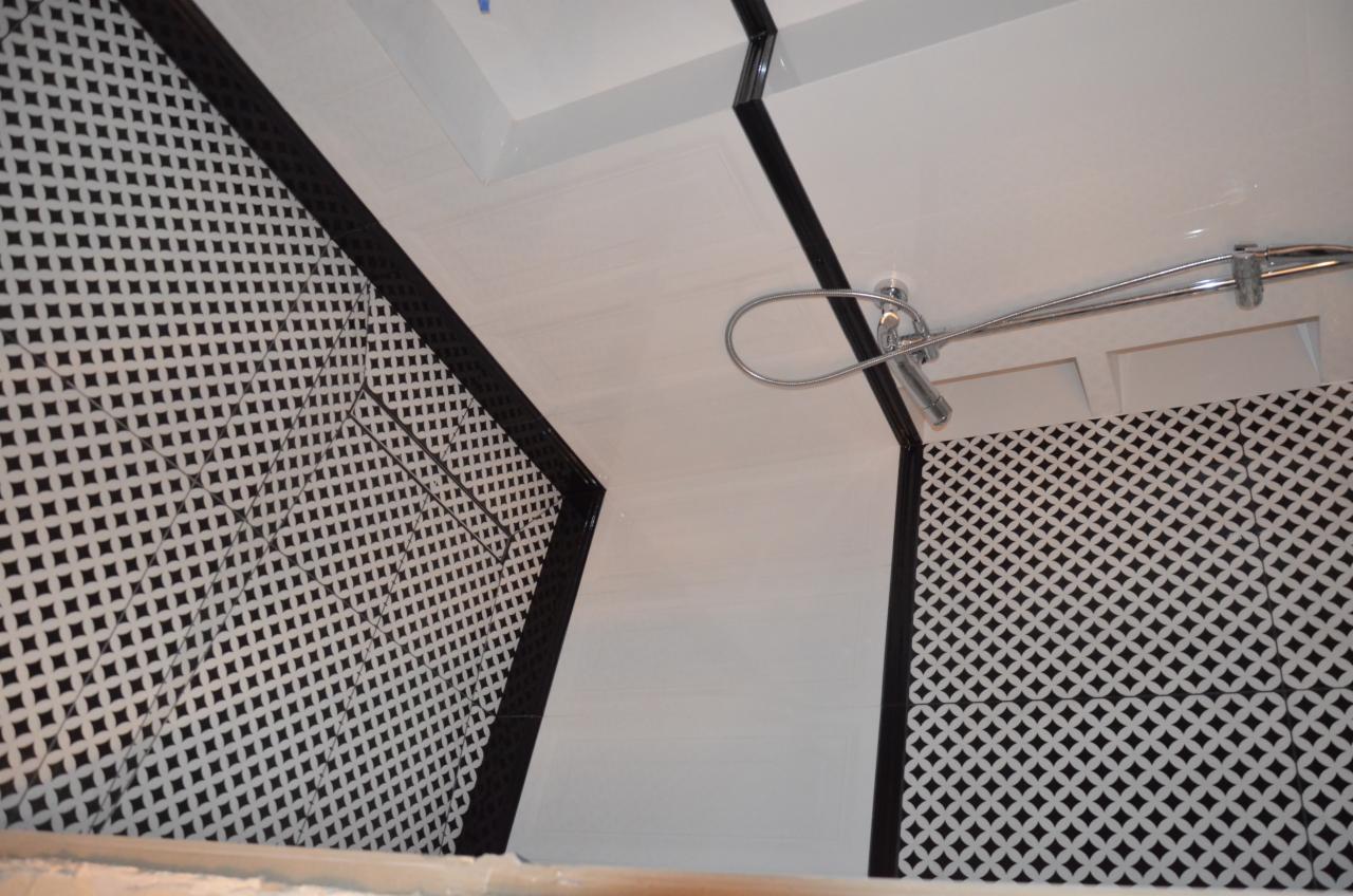 Wykończona łazienka z biało-czarnymi płytkami w geometryczny wzór, chromowaną armaturą prysznicową i białym sufitem z czarnymi listwami dekoracyjnymi