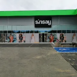 Zewnętrzna reklama na szklanej fasadzie sklepu Sinsay, prezentująca fotorealistyczne wydruki w oknach z wizerunkami modelek w różnych stylizacjach, widoczne z parkingu.