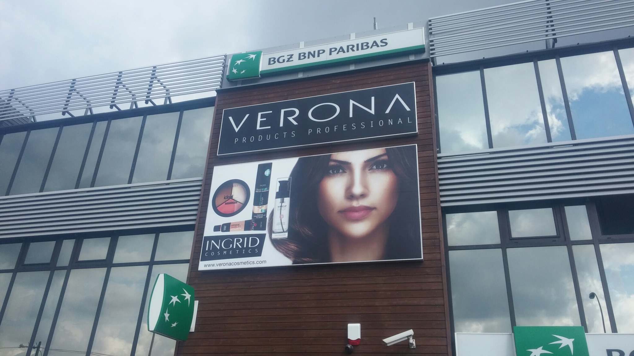 Elewacja budynku z kasetonami reklamowymi BGZ BNP Paribas, Verona Products Professional oraz Ingrid Cosmetics, kamera przemysłowa i sygnalizator alarmowy.
