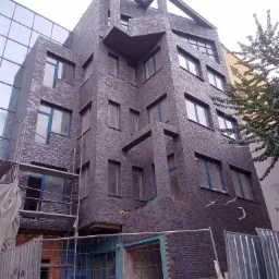 Wielopiętrowy budynek w trakcie wznoszenia elewacji z klinkieru w systemie ISO-KLINK-PUR, widoczne rusztowania i zabezpieczenia budowy.