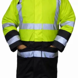 Mężczyzna w długiej, ocieplanej kurtce roboczej w kolorze jaskrawej żółci z czarnym dołem i odblaskowymi pasami, z kapturem na głowie i rękami w kieszeniach.