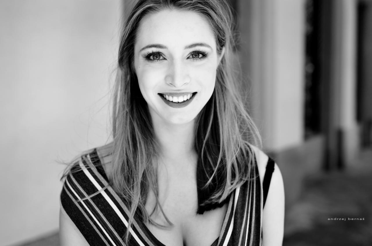 Portret uśmiechniętej kobiety w sukience w paski, czarno-białe zdjęcie z wyraźnym oświetleniem i głębią ostrości.