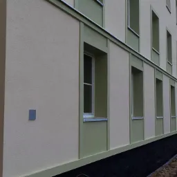 Elewacja budynku po ociepleniu z widocznymi oknami i fragmentem fundamentu, na pierwszym planie ziemia i wykop.