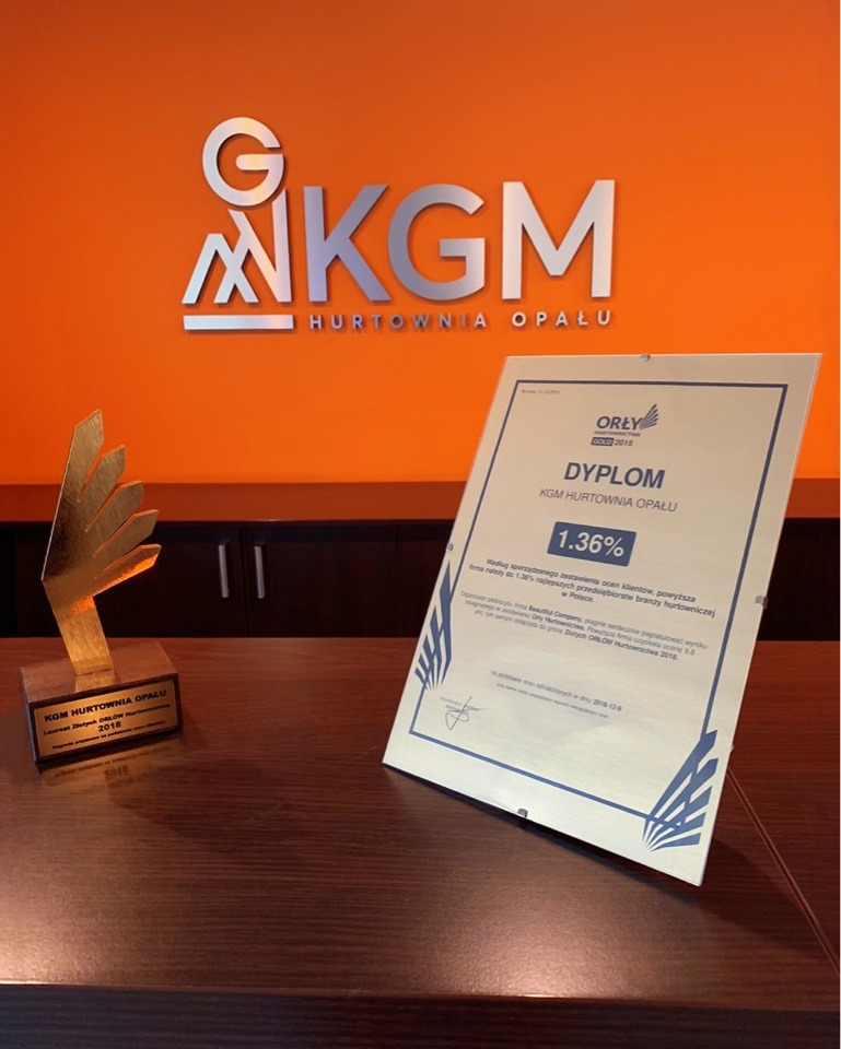 Nagroda i dyplom dla KGM Hurtownia Opału na ciemnym biurku, pomarańczowe tło z logo firmy.