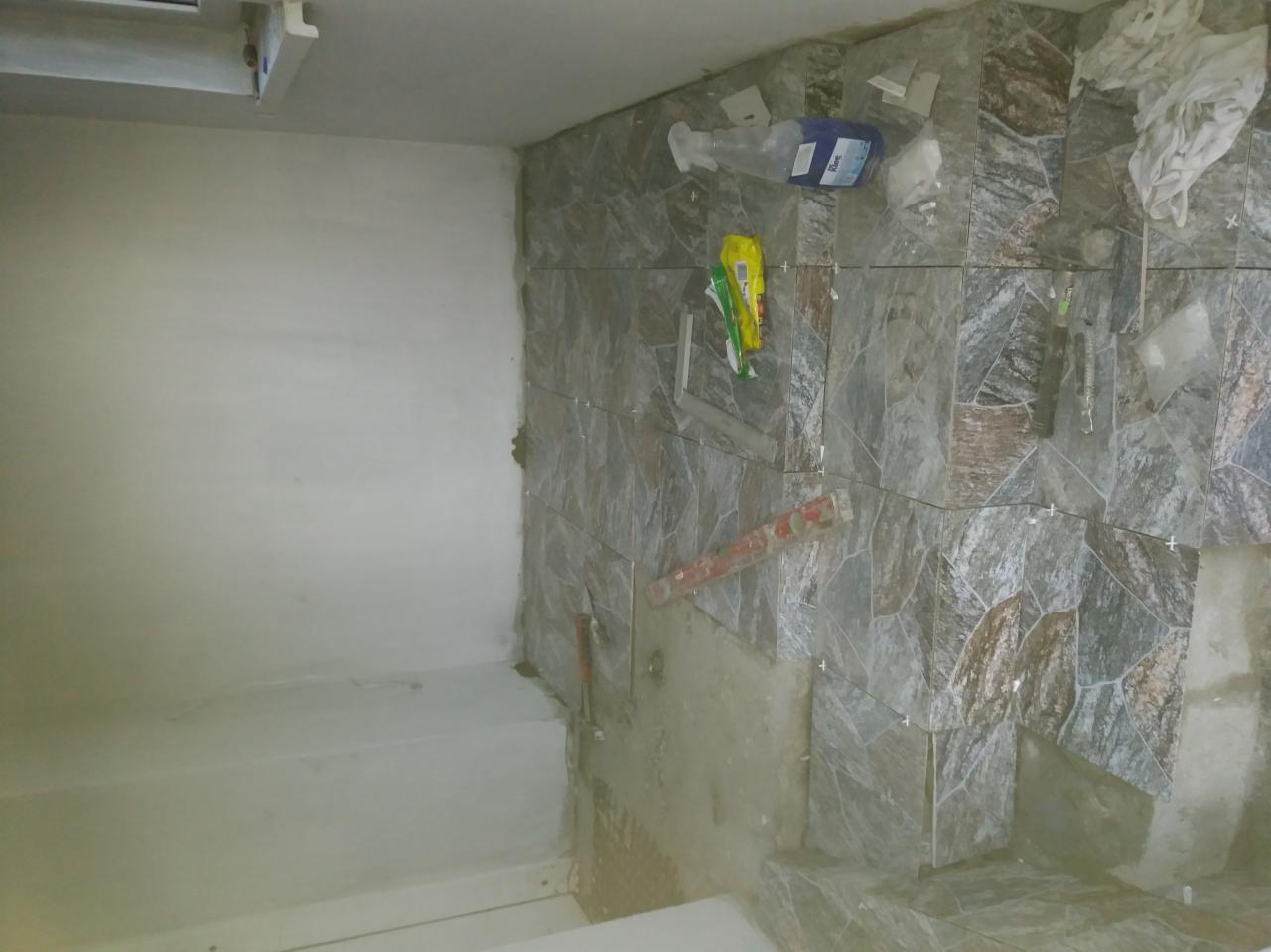 W trakcie układania płytek imitujących kamień na ścianie w łazience. Widoczne narzędzia, poziomica, opakowanie po kleju i krzyżyki dystansowe.