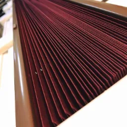 Plisowana zasłona w kolorze burgundowym, zamontowana w brązowej ramie okiennej, widok z bliska pod kątem.