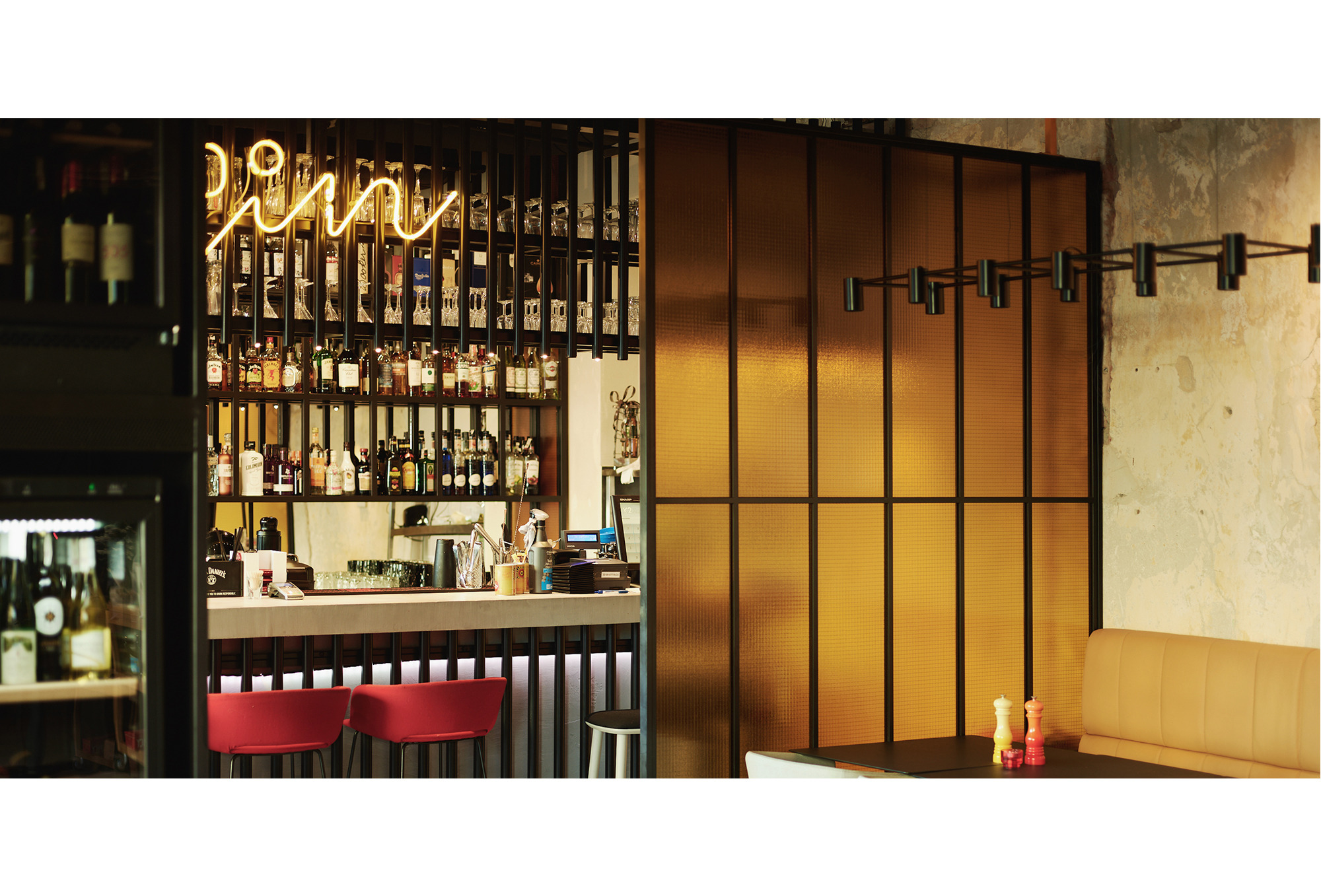 Wnętrze restauracji Pop-Inn w Gdyni, widok na bar z podświetlonym neonem, regały z butelkami alkoholu i stoliki z krzesłami.