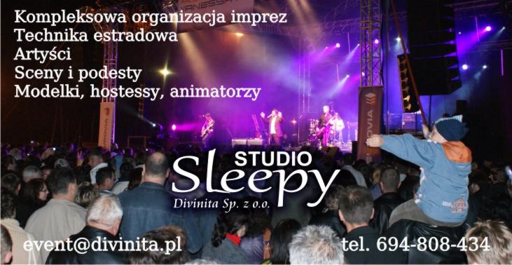 Koncert z oświetleniem scenicznym i publicznością, widoczny zespół na scenie, tłum ludzi i logo firmy organizującej wydarzenie.