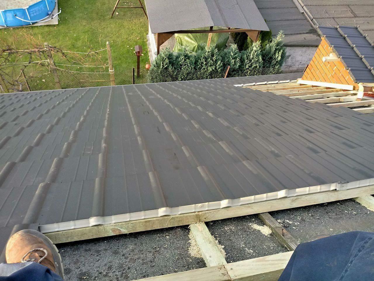 Montaż paneli dachowych z widoczną konstrukcją drewnianą, fragmentem buta i widokiem na ogród w tle.