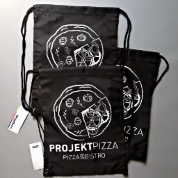 Trzy czarne worki ze sznurkiem, z białym nadrukiem pizzy z elementami mechanicznymi oraz napisem 'PROJEKTPIZZA PIZZA&BISTRO', leżące na szarym tle.