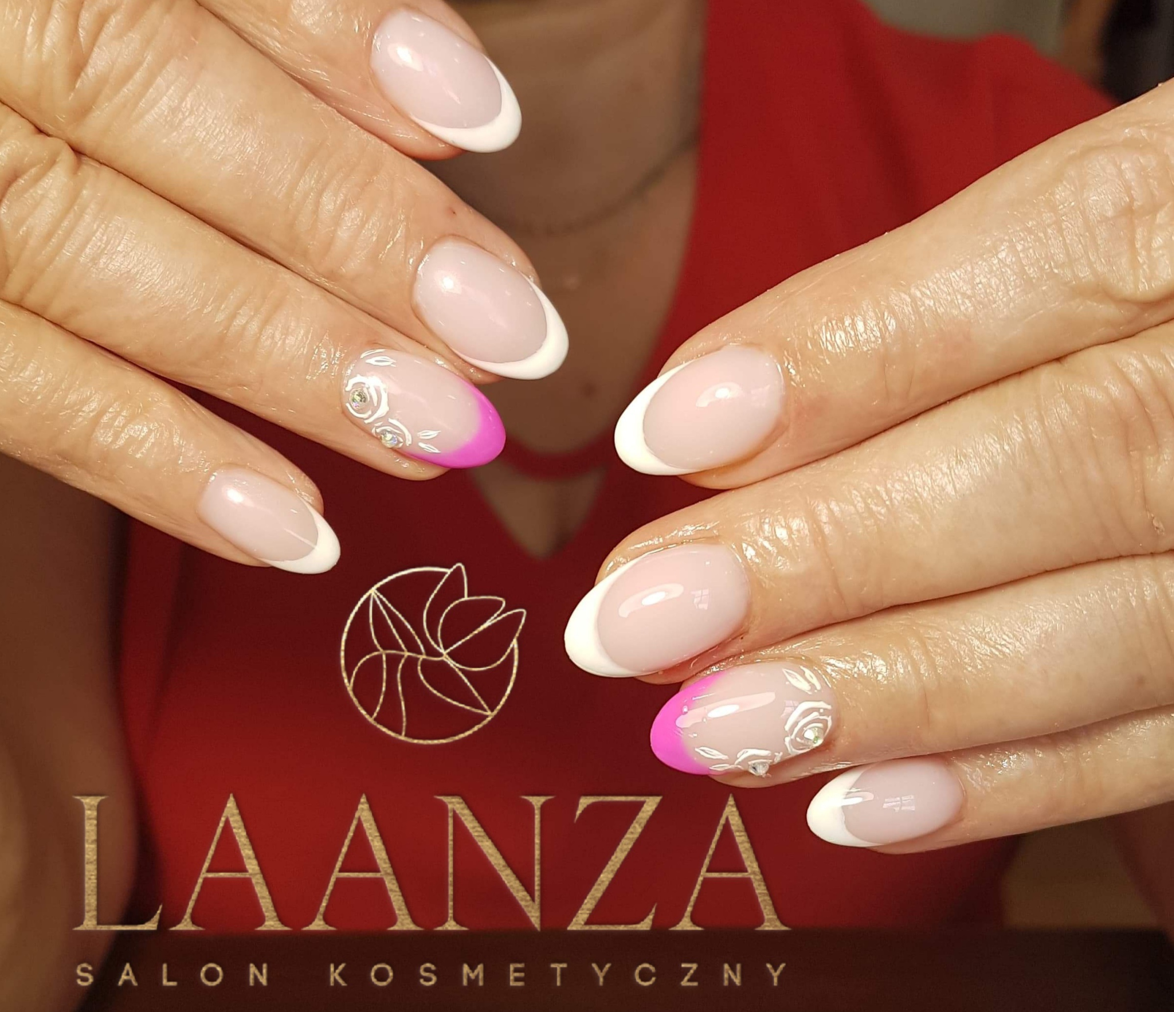 Dłonie z owalnymi paznokciami french manicure z różowym akcentem i białymi kwiatowymi zdobieniami na tle bordowego logo salonu kosmetycznego.