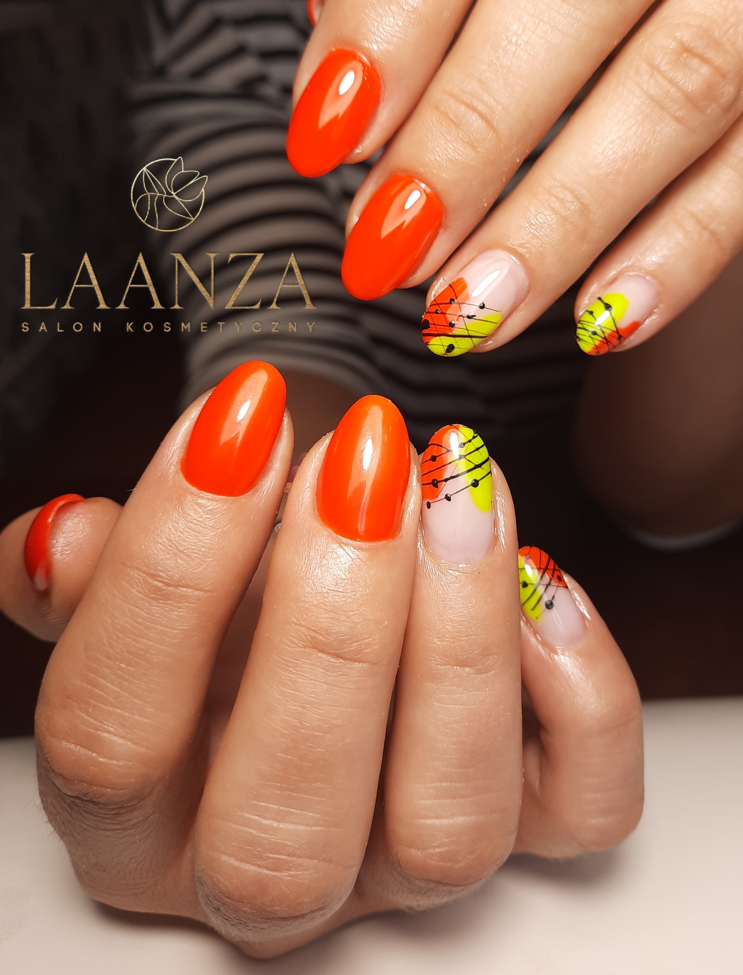 Pomarańczowe paznokcie w kształcie migdała oraz paznokcie z abstrakcyjnym zdobieniem w kolorach neonowej zieleni, pomarańczy i czarnych kropek, na tle logo salonu kosmetycznego Laanza.