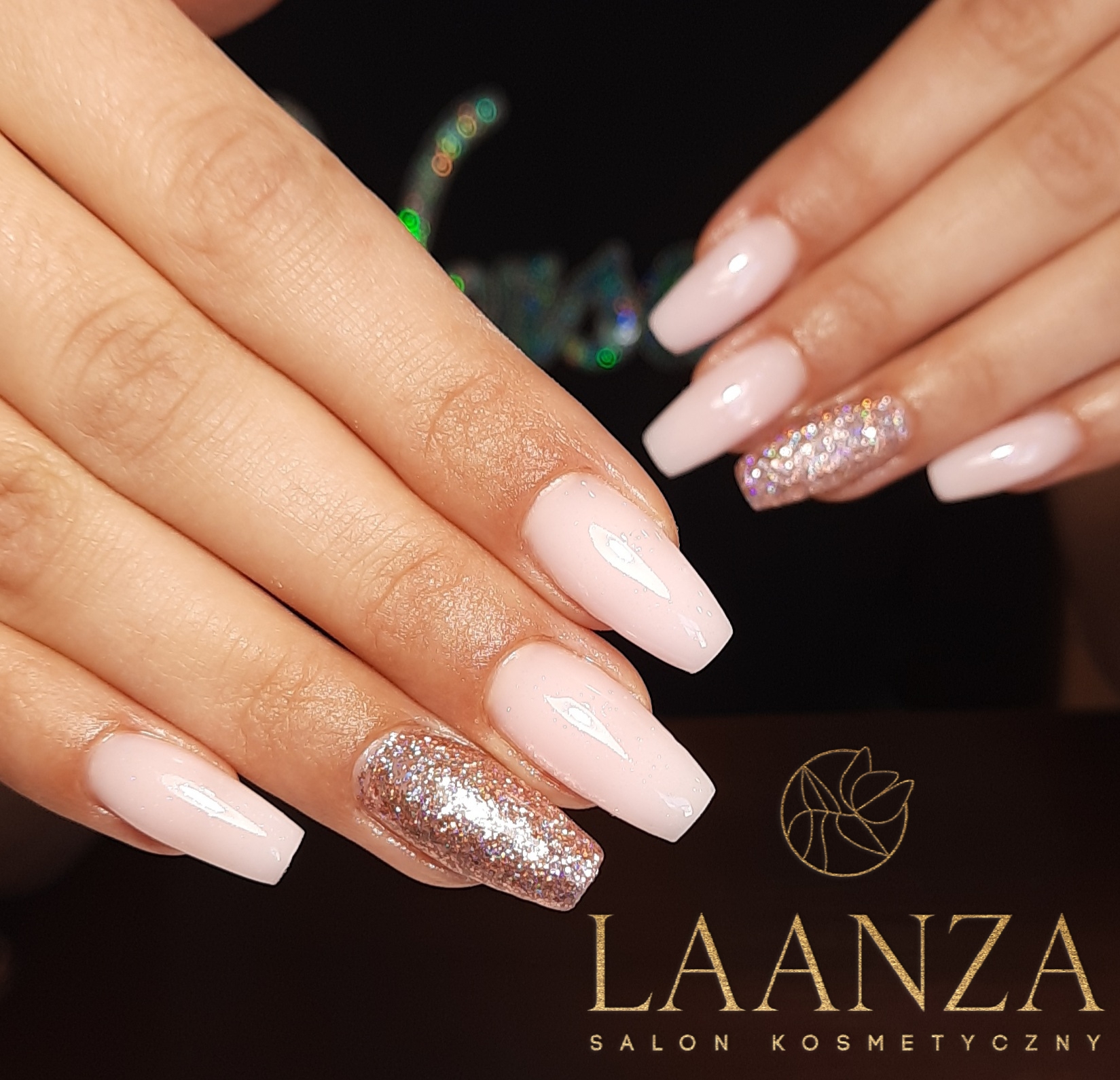 Dłonie z jasnoróżowym, kwadratowym manicure, jeden paznokieć każdej dłoni pokryty brokatem, widoczne logo salonu kosmetycznego w tle.