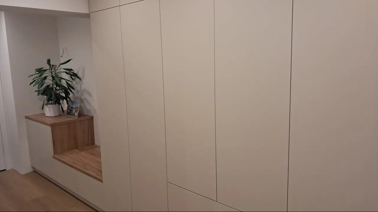 Jasna zabudowa wnęki z siedziskiem z drewnianym blatem, na którym stoi roślina doniczkowa i ramka ze zdjęciem. Minimalistyczny design, gładkie fronty szaf.