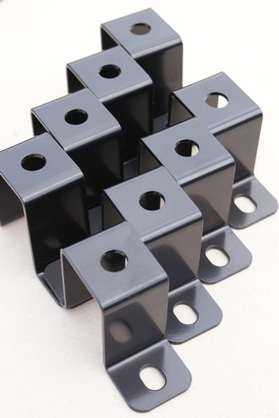 Seria identycznych, czarnych, stalowych uchwytów kątowych z otworami, ułożonych w regularny wzór na jasnym tle.