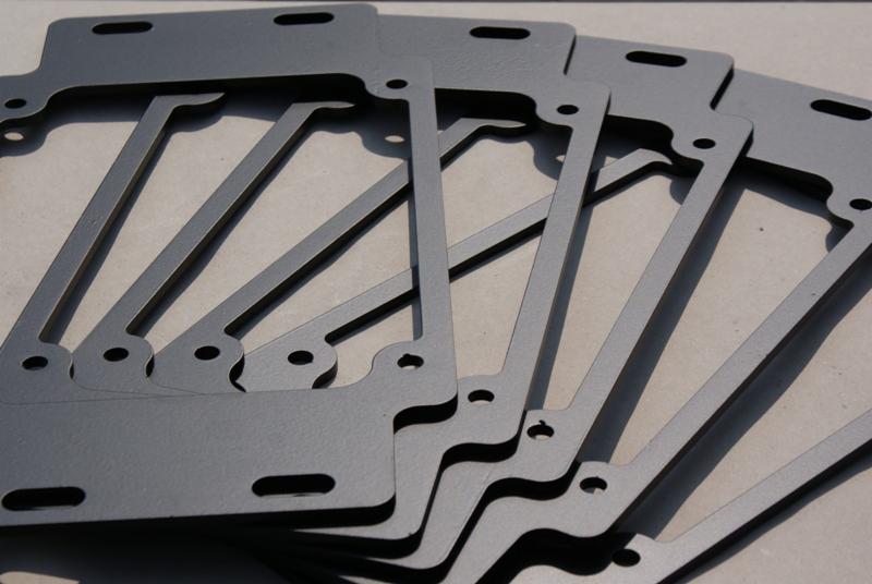 Stos szarych, metalowych ramek o nieregularnym kształcie, przypominających elementy konstrukcyjne, z widocznymi otworami montażowymi.