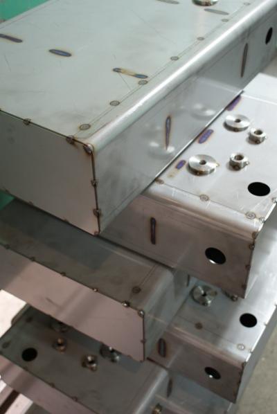 Stos metalowych, spawanych skrzynek z widocznymi śladami spawania i otworami montażowymi.