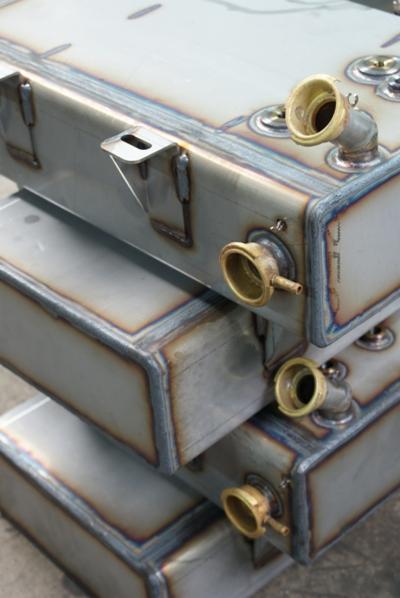 Stos zbiorników metalowych z widocznymi spawami i mosiężnymi króćcami, z mocowaniami na górnym zbiorniku.