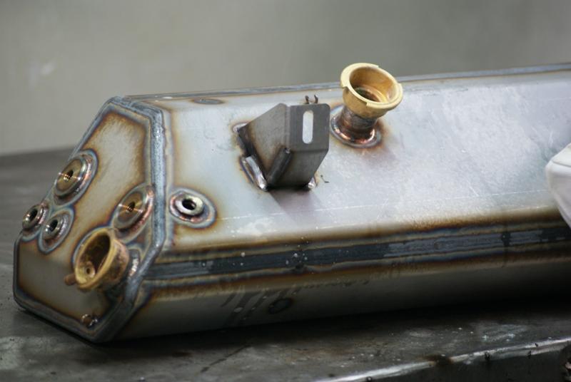 Metalowy zbiornik z widocznymi spawami i przyłączami, uchwyt przyspawany na górze, ślady po spawaniu widoczne na powierzchni.