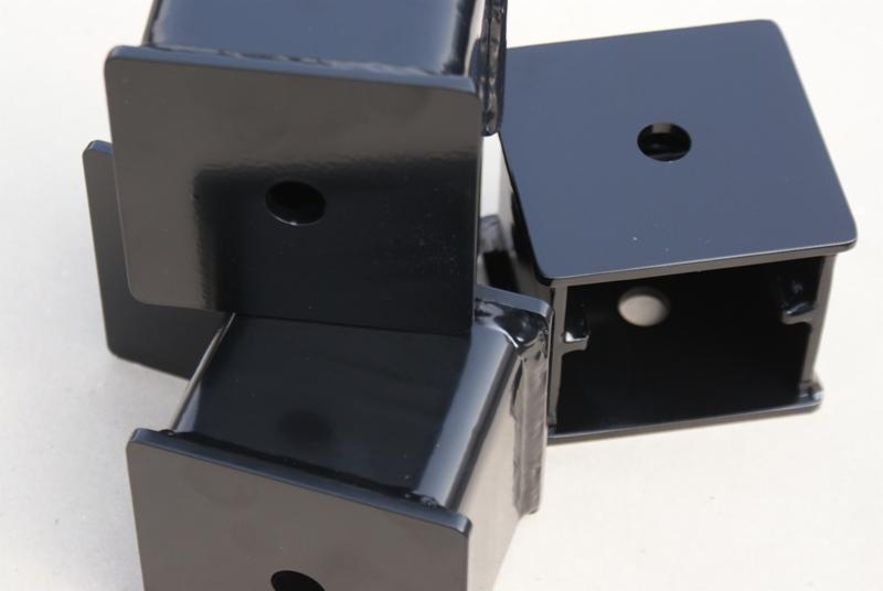 Cztery czarne, błyszczące, spawane elementy metalowe o kształcie prostopadłościanu z otworem na górnej powierzchni, ułożone na jasnym tle.