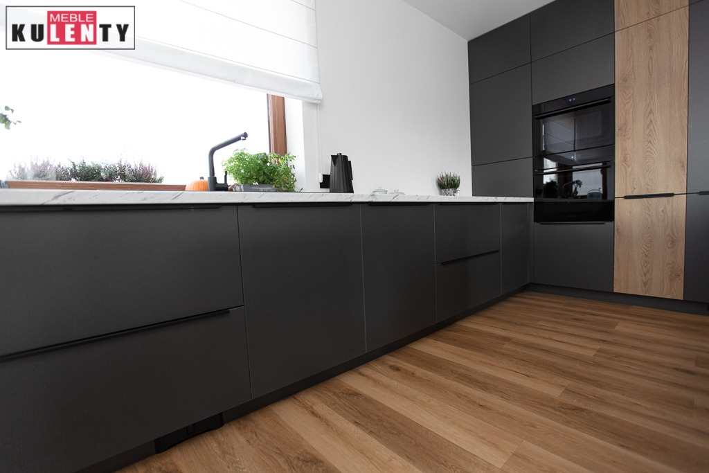 Nowoczesna, ciemnoszara kuchnia z drewnianymi akcentami, blatem z efektem marmuru, minimalistyczną armaturą i roślinami w oknie, widziana z niskiego kąta.