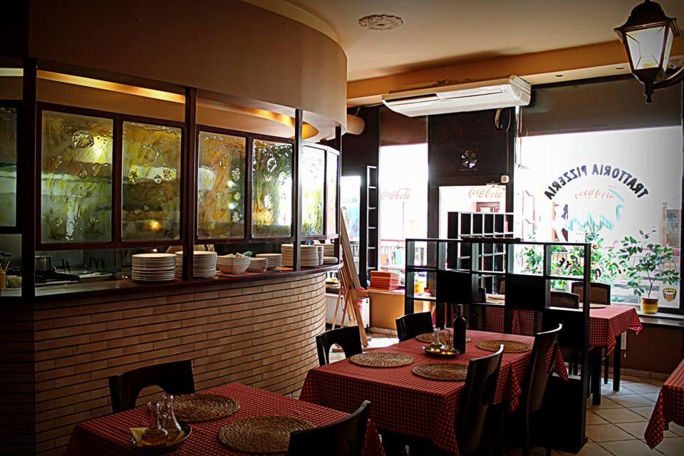 Wnętrze restauracji z ceglanym barem, szklanymi panelami z abstrakcyjnym wzorem, zastawionymi stołami z czerwoną kratą i widoczną kuchnią w tle.