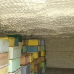 Wnętrze magazynu z ocieplonym sufitem i ścianami, obok ułożone w stosy kolorowe ule.