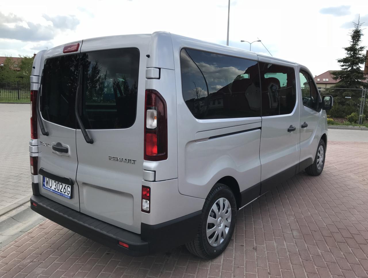 Srebrny Renault Trafic z przyciemnianymi szybami, widok z tyłu na brukowanym parkingu, tablica rejestracyjna WU 3026G.
