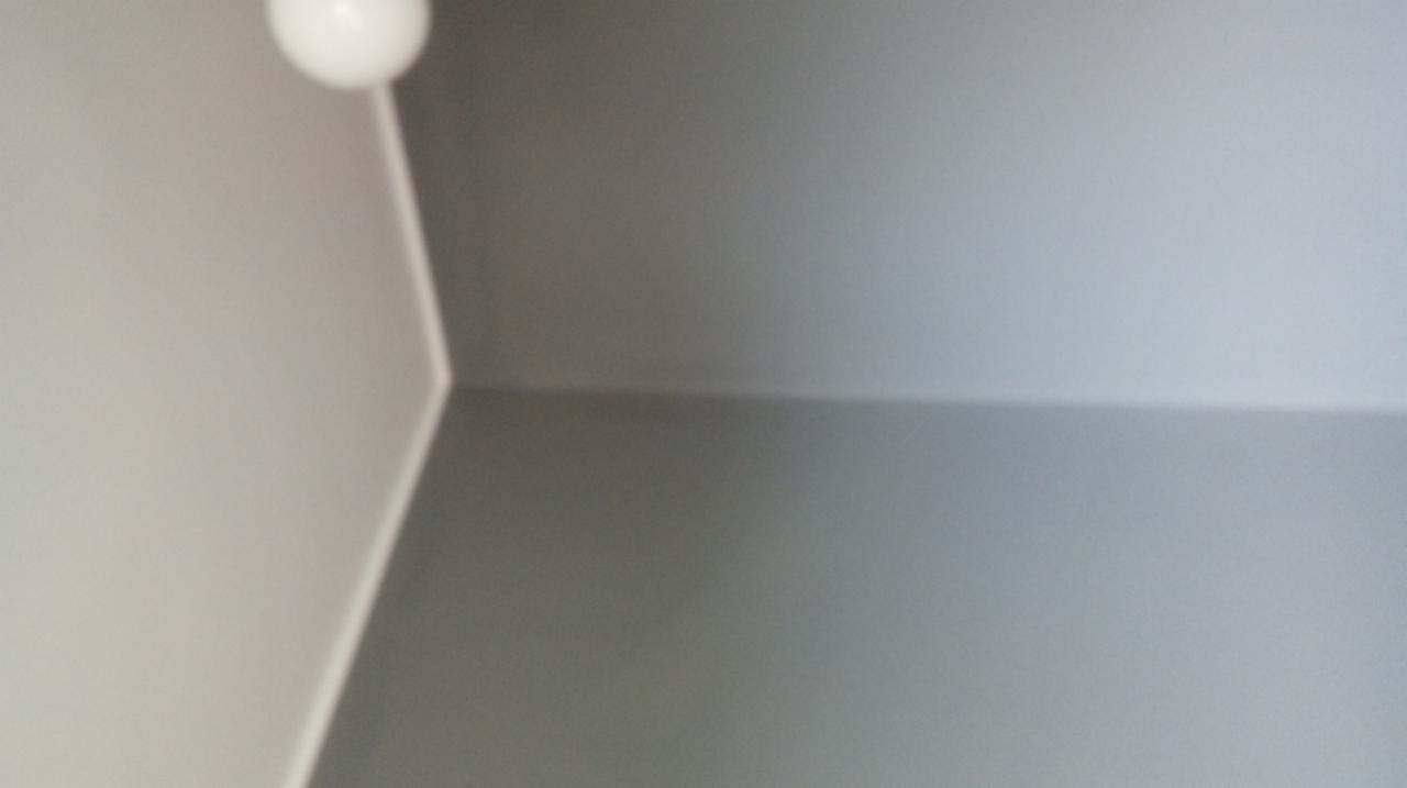 Świeżo pomalowany narożnik pokoju, z widoczną lampą sufitową w lewym górnym rogu, gdzie ściany w odcieniach szarości spotykają się pod kątem prostym.