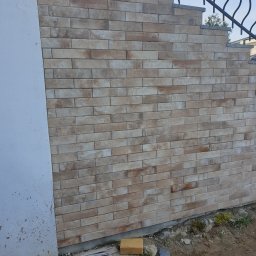 Sławomir Michalski - Elewacja z cegiełek klinkierowych w odcieniach beżu i brązu, fragment schodów z metalową balustradą w tle, widok z dołu.