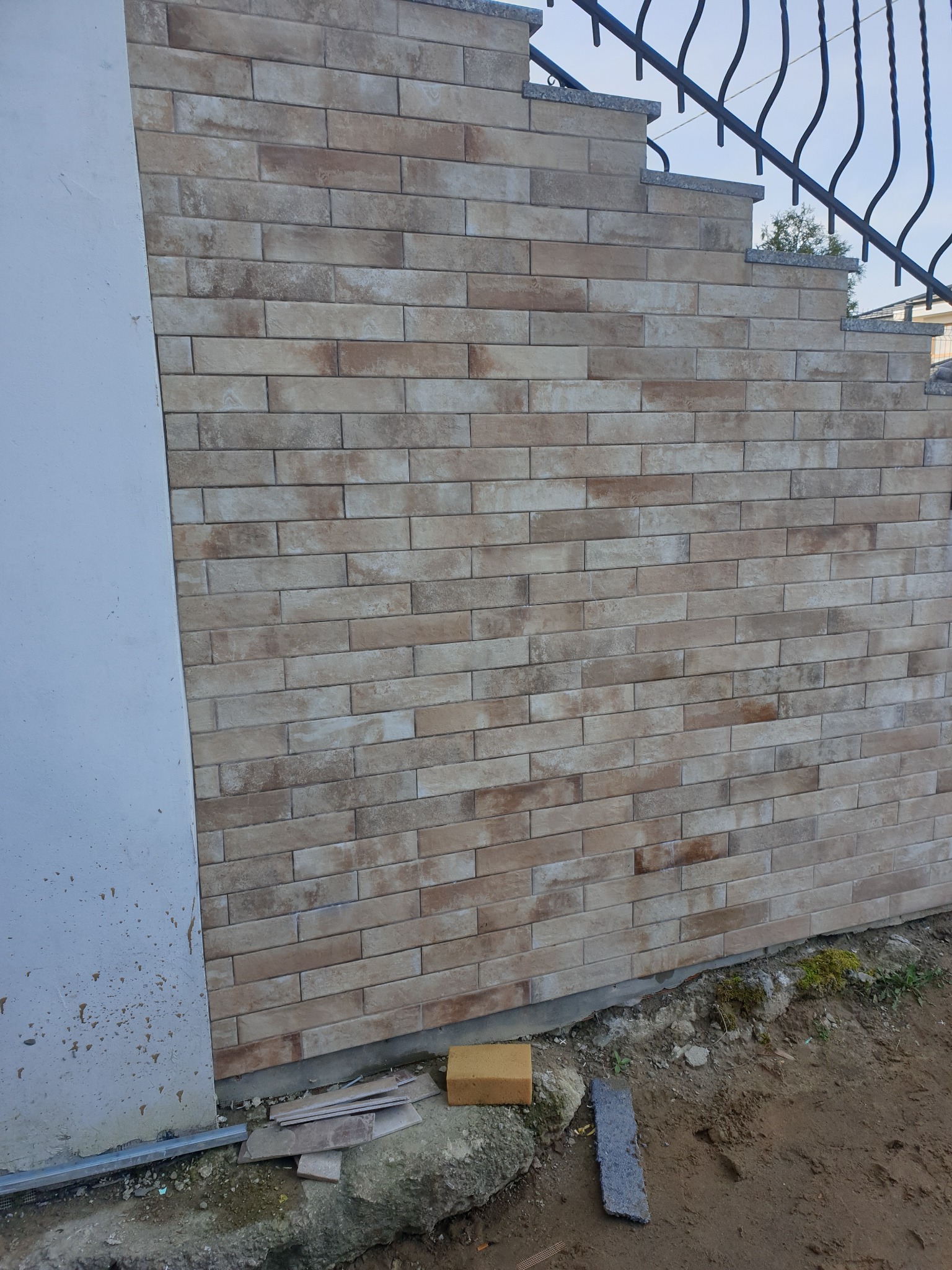 Elewacja z cegiełek klinkierowych w odcieniach beżu i brązu, fragment schodów z metalową balustradą w tle, widok z dołu.