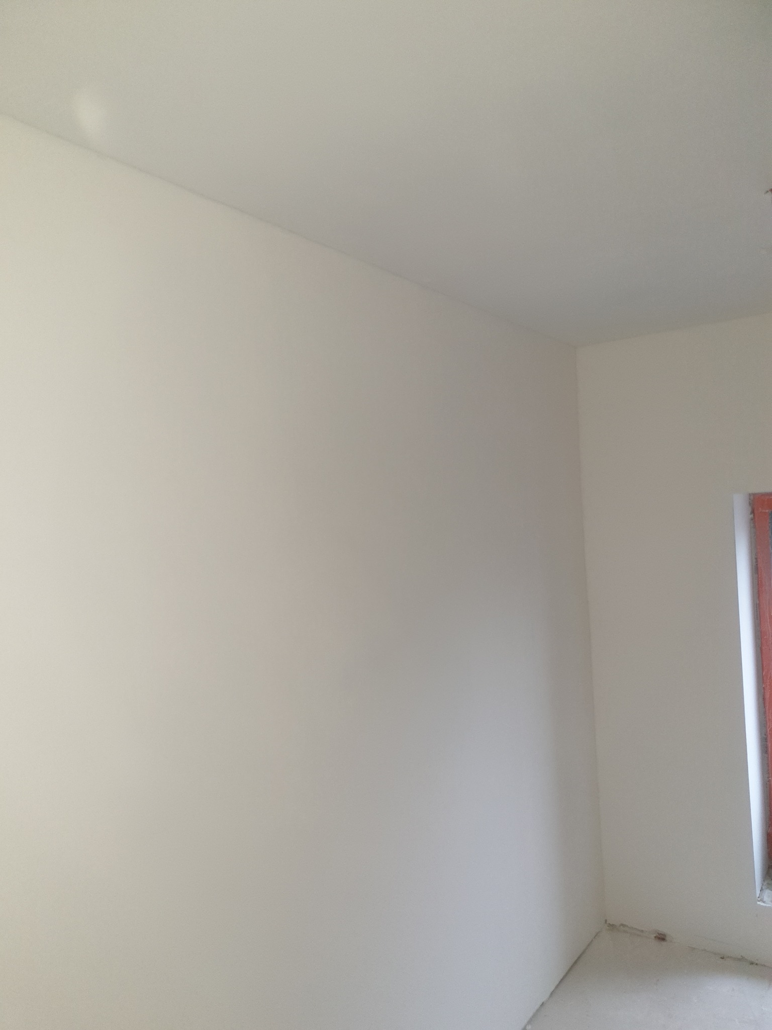 Wnętrze po remoncie: gładkie, białe ściany i sufit, widoczny fragment okna z czerwoną ramą. Minimalistyczny kadr, skupiający się na jakości wykończenia.