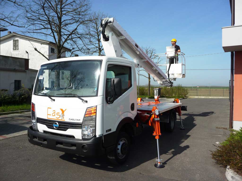 Biały samochód z podnośnikiem koszowym na wysięgniku, operator w kasku na platformie, podpory rozłożone, logo 'Easy' na kabinie, budynek w tle.