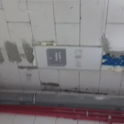 Montaż podtynkowego rozdzielacza elektrycznego w surowym stanie, widoczne przewody w niebieskiej peszli, rury instalacyjne i ślady po zaprawie na bloczkach z betonu komórkowego.