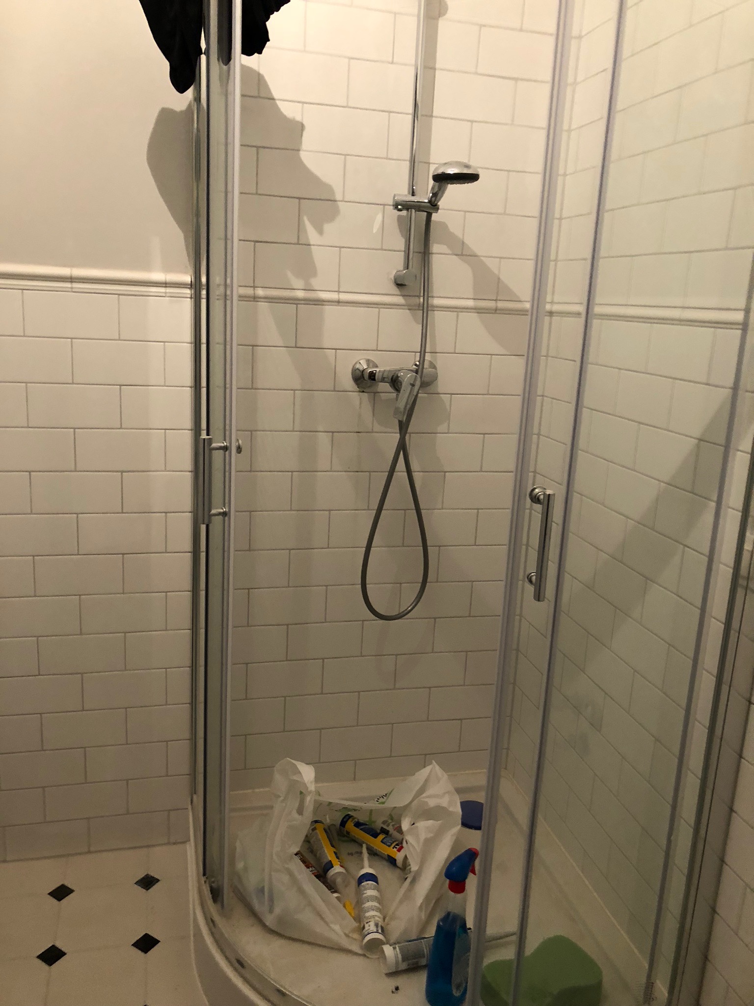 Kabina prysznicowa z białymi płytkami, widoczne silikony i środki czystości wewnątrz, sugerujące prace wykończeniowe lub sprzątanie po remoncie.