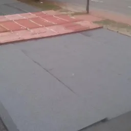 Fragment dachu z częściowo ułożoną papą termozgrzewalną i pozostawioną starą dachówką, palnik dekarski w lewym dolnym rogu, widok z góry.