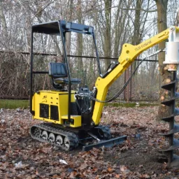 Żółta gąsienicowa maszyna z wiertłem TUR Poland wierci otwór w ziemi przy drzewie na tle jesiennego lasu.