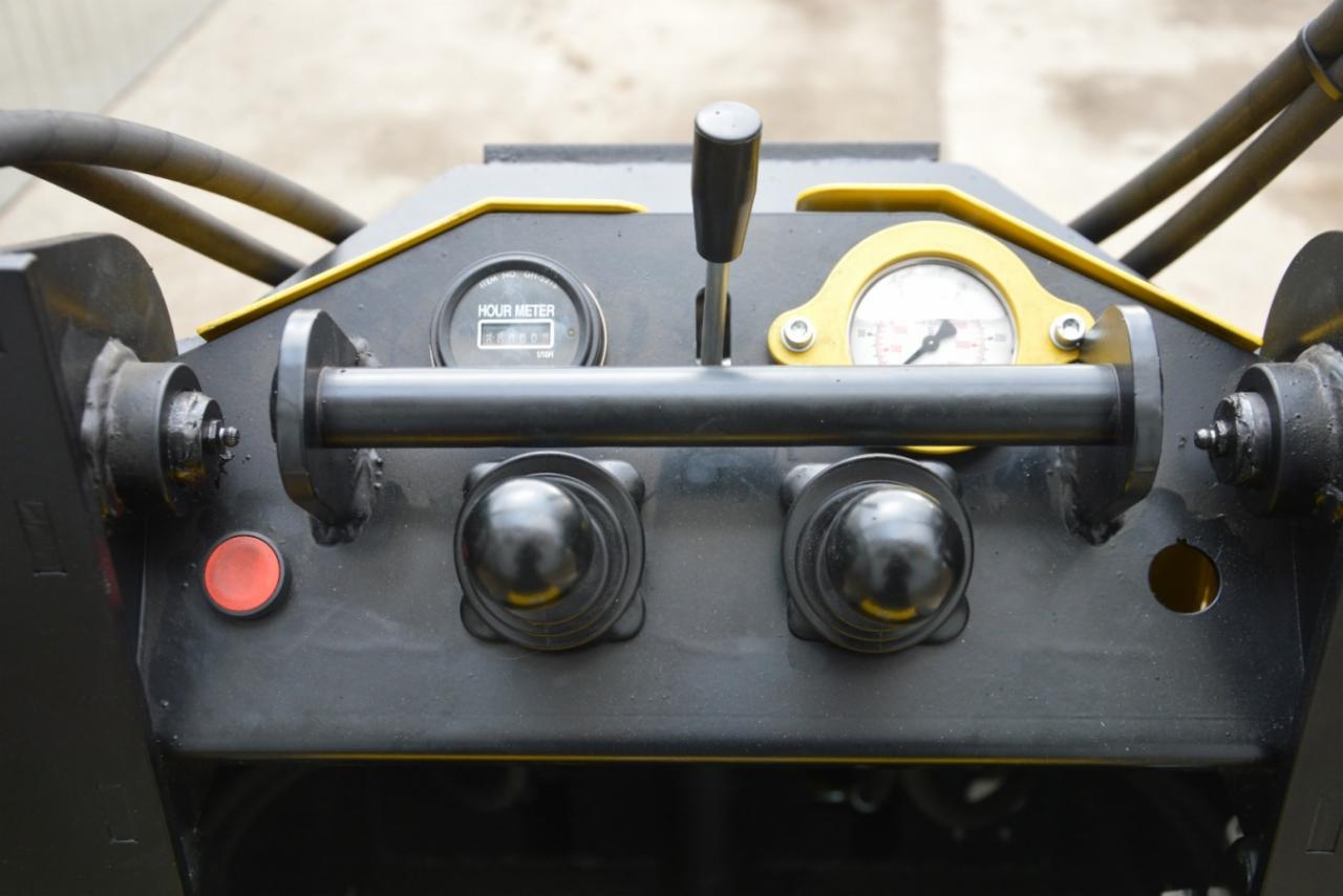 Panel sterowania maszyny budowlanej z licznikiem motogodzin, manometrem i dźwignią zmiany biegów, utrzymany w czarno-żółtej kolorystyce.