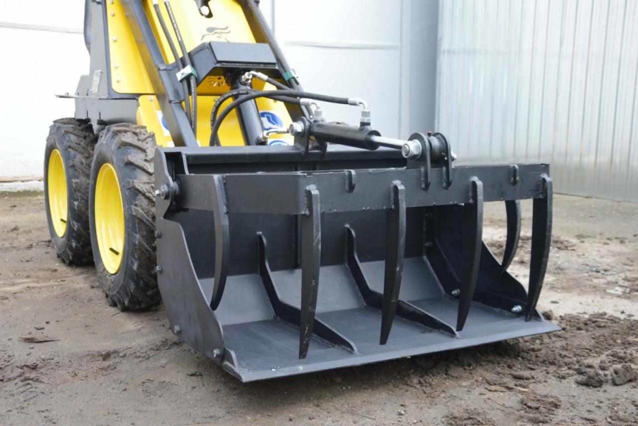 Żółta maszyna z czarnym osprzętem do spulchniania ziemi, widok z przodu, lekko zabrudzone opony.