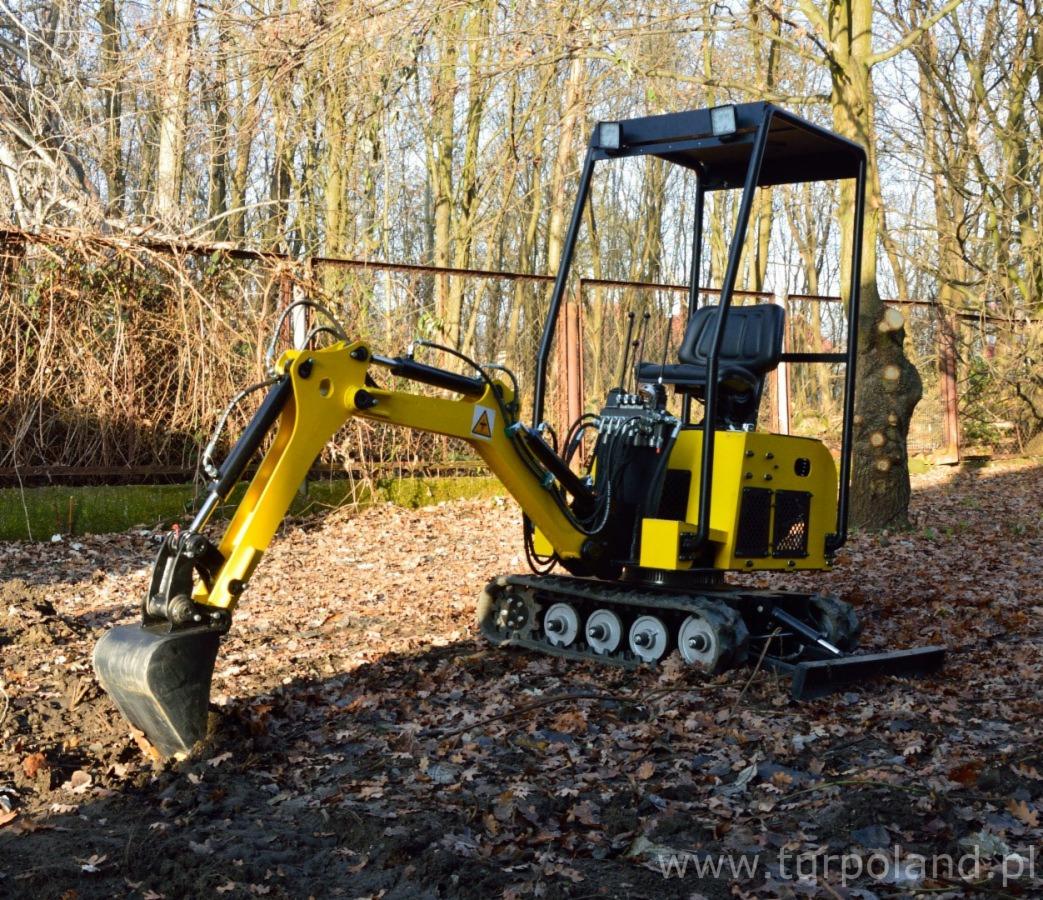 Kompaktowa, żółto-czarna maszyna budowlana z łyżką kopiącą w ziemi, otoczona liśćmi i drzewami.