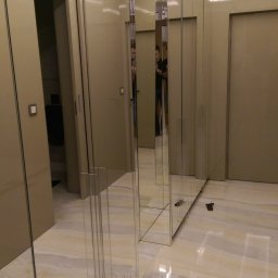 TOTAL RENOVATIONS SPÓŁKA Z OGRANICZONĄ ODPOWIEDZIALNOŚCIĄ - Nowoczesna szafa wnękowa z lustrzanymi frontami, wkomponowana w korytarz z marmurową podłogą. Widoczne odbicie osoby w lustrze.