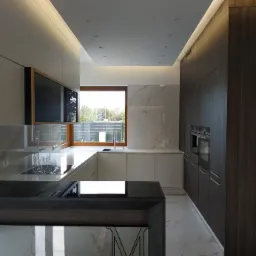 Nowoczesna kuchnia: białe i grafitowe szafki, marmurowe blaty i podłoga, okno z widokiem na zieleń. Oświetlenie sufitowe i listwy LED. Minimalistyczny design.