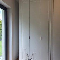 TOTAL RENOVATIONS SPÓŁKA Z OGRANICZONĄ ODPOWIEDZIALNOŚCIĄ - Elegancka, szara szafa wnękowa z frezowanymi drzwiami, dopasowana do listwy sufitowej, z widocznym fragmentem okna i podłogi. Minimalistyczne uchwyty.