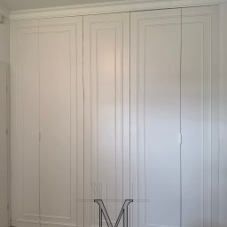 TOTAL RENOVATIONS SPÓŁKA Z OGRANICZONĄ ODPOWIEDZIALNOŚCIĄ - Biała, trzydrzwiowa szafa wnękowa z dekoracyjnymi frezami na frontach, dopasowana do listwy przysufitowej. Na dole widoczna drewniana podłoga.