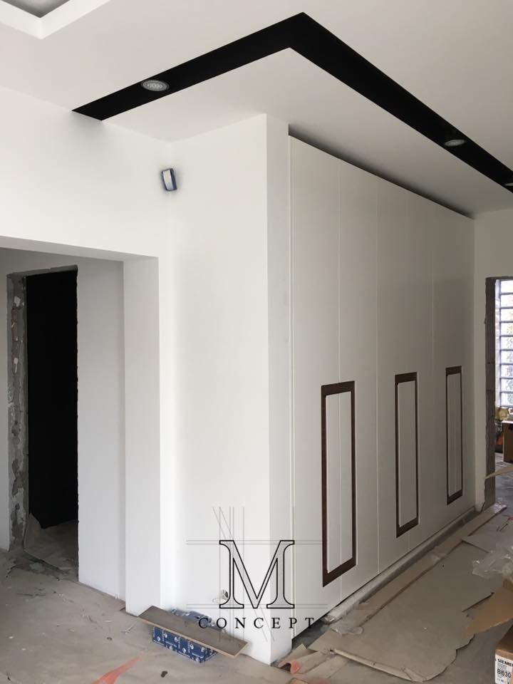 Biała szafa wnękowa z ciemnymi, prostokątnymi wstawkami na frontach, w jasnym wnętrzu z czarnymi elementami dekoracyjnymi na suficie.