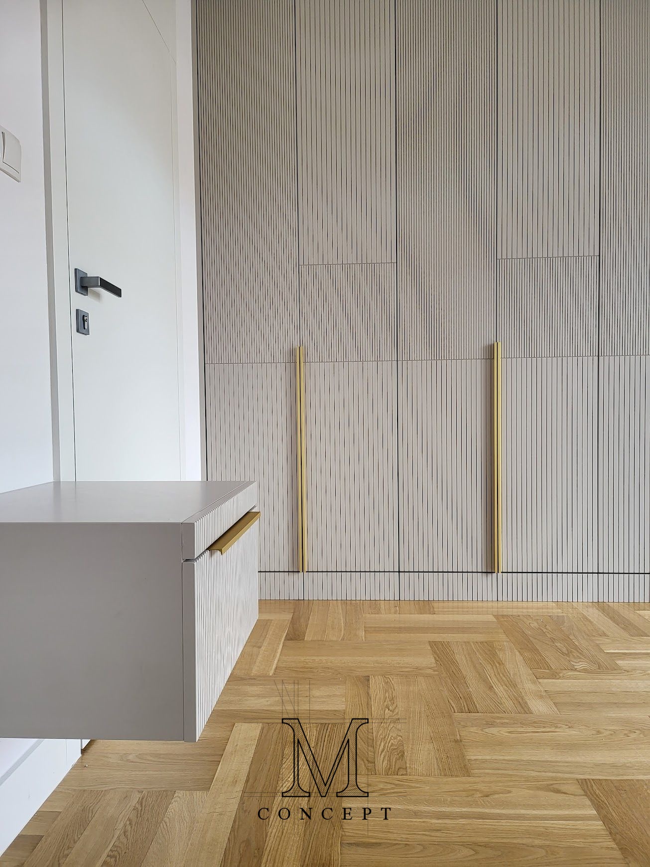Nowoczesna szafa wnękowa z ryflowanymi frontami i złotymi uchwytami, uzupełniona wiszącą szafką i parkietem w jodełkę. Minimalistyczny design.