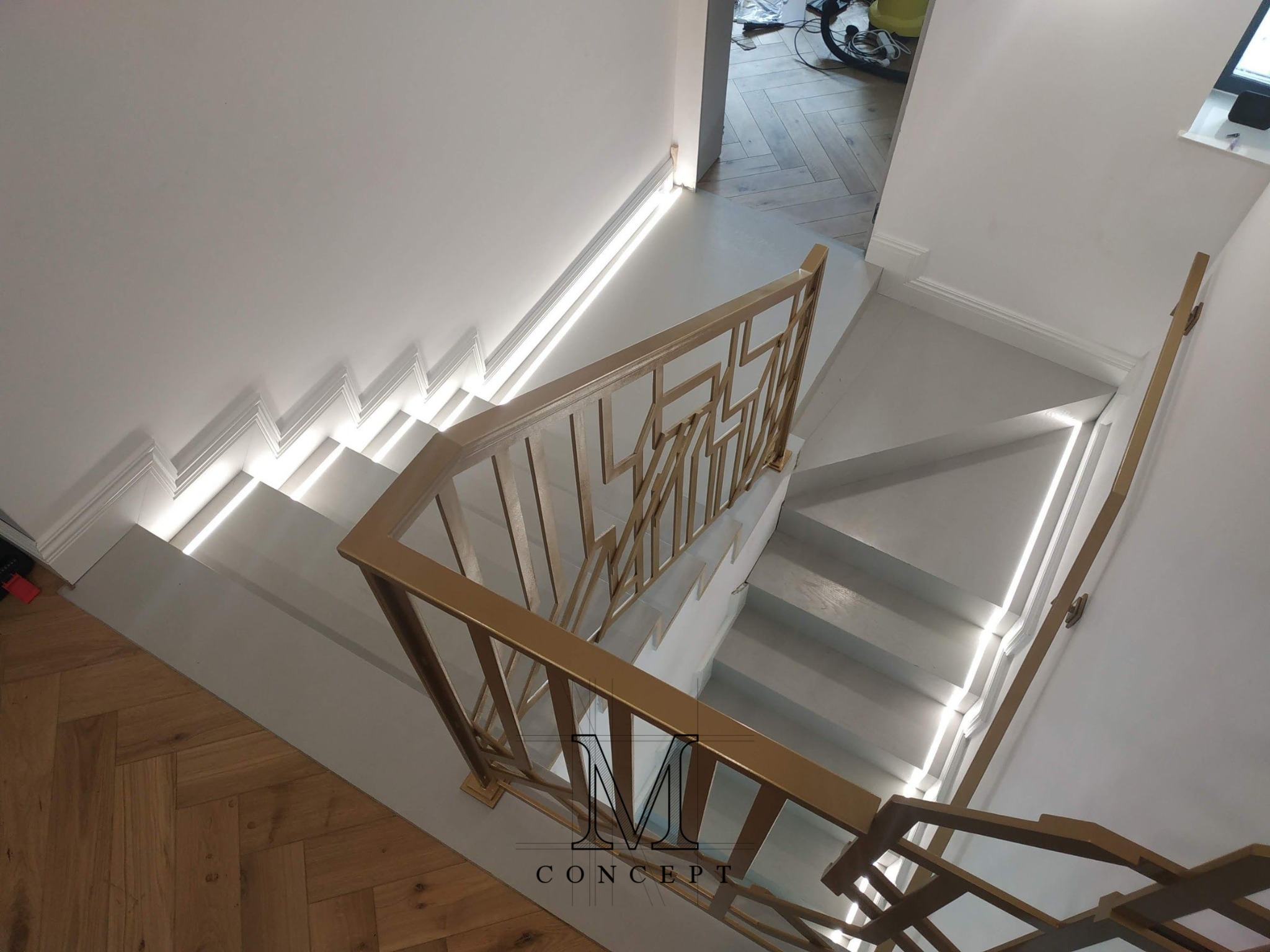 Nowoczesne schody z oświetleniem LED i złotą balustradą, widok z góry. Parkiet w jodełkę, minimalistyczny design, listwy przyścienne.