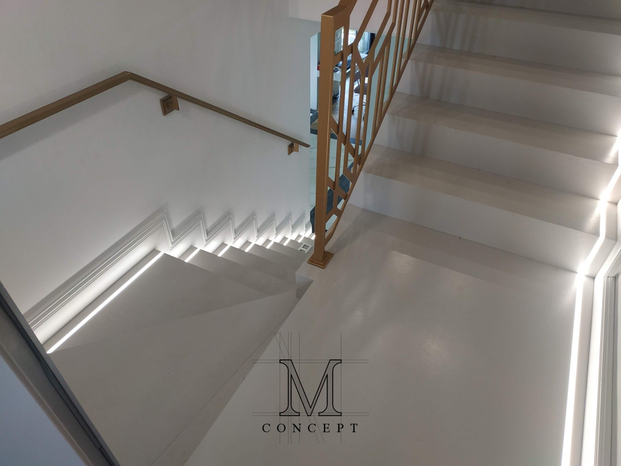 Nowoczesne, białe schody z oświetleniem LED i złotą, geometryczną balustradą. Widok z góry, podkreślający minimalizm i precyzję wykonania.